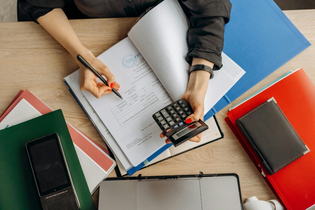 A person examining documents on a table, holding a calculator.