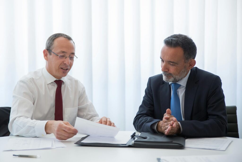 Two businessmen engaged in a serious conversation, one holding a document—capturing the negotiation and planning phase of structuring a business sale with installment tax treatment.