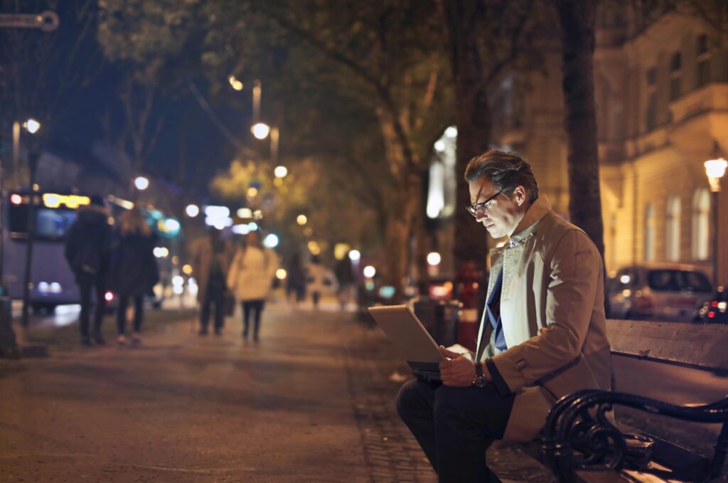A man in a brown coat sits on a park bench working on a MacBook, symbolizing expats managing international taxes and foreign tax credit carryovers.
