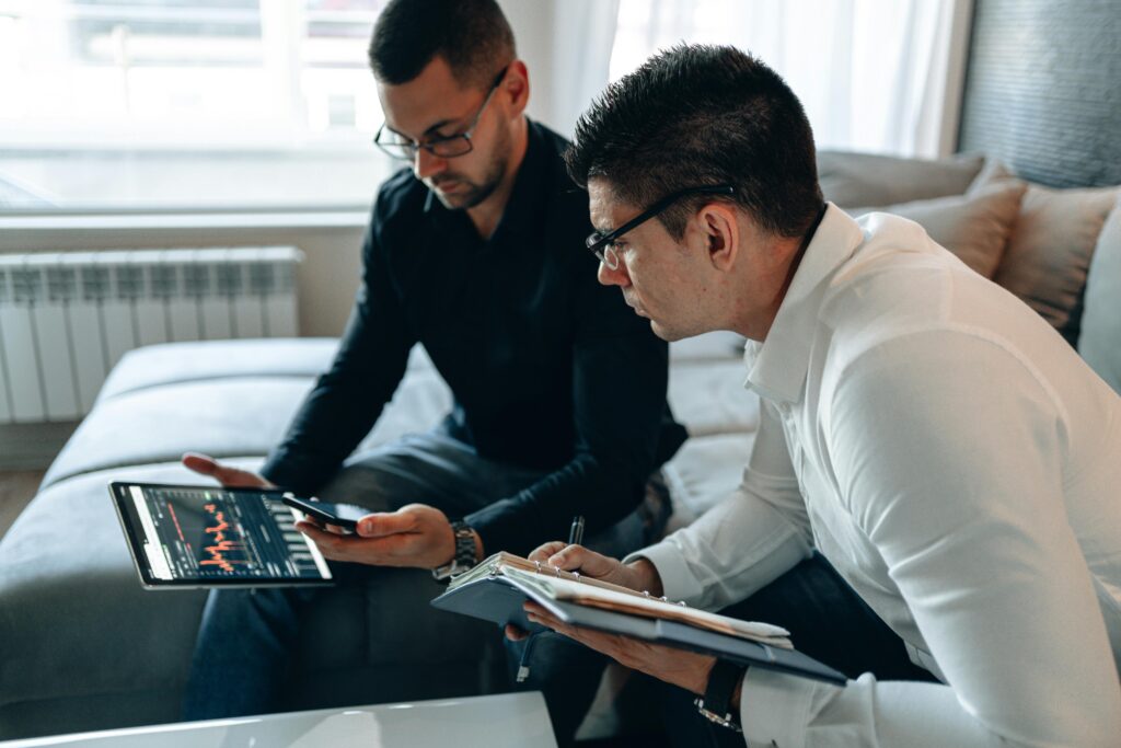 Two traders reviewing cryptocurrency tax data on a tablet, representing 2025 crypto tax rules and the upcoming wash sale changes.