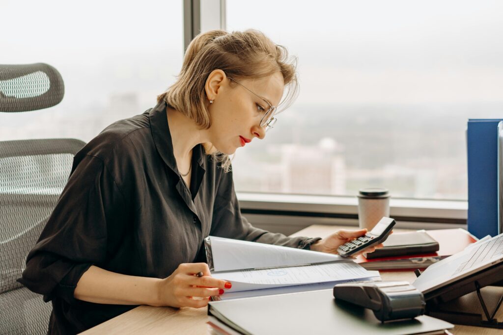 Woman using a calculator while preparing financial documents, illustrating how to report Treasury bill income on federal tax returns.
