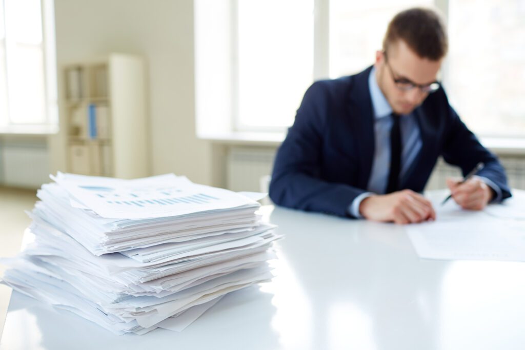 Image of a person sitting at a desk next to a pile of paperwork.