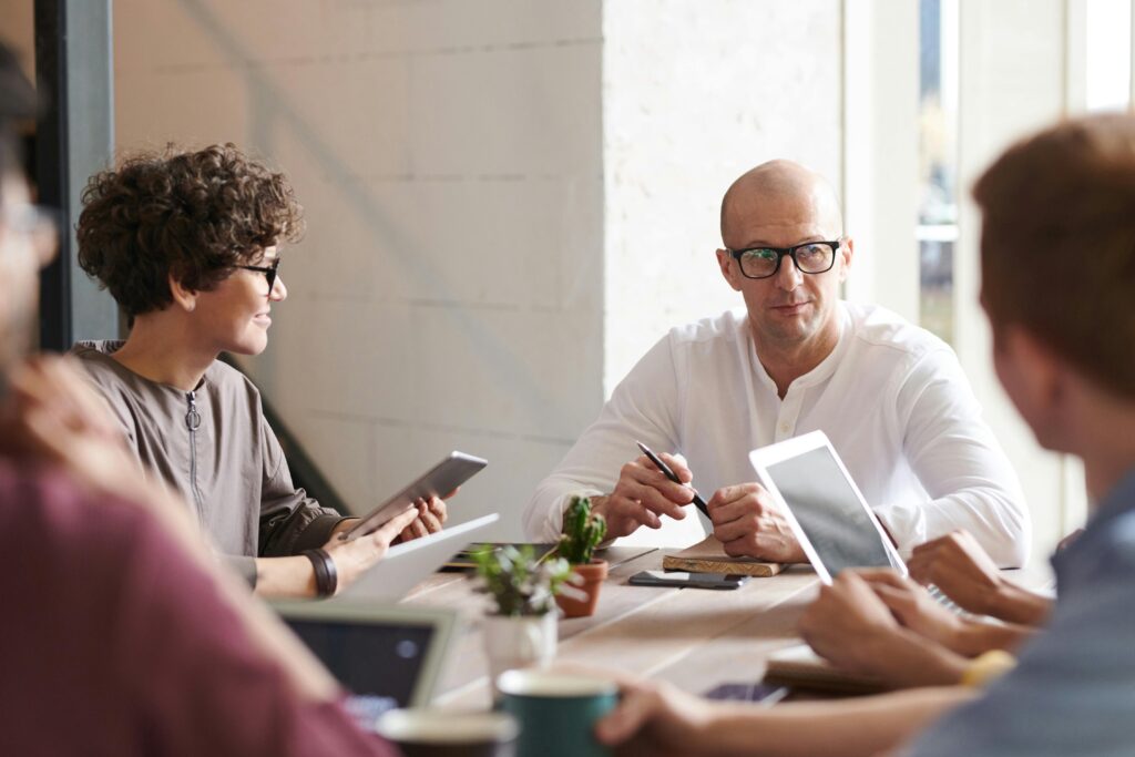Photo of a man sitting in front of a group of people, seemingly engaged in a discussion or presentation.